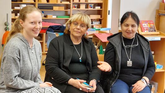 Drei Frauen sitzen und unterhalten sich in einem Klassenzimmer, eine von ihnen lächelt in die Kamera.