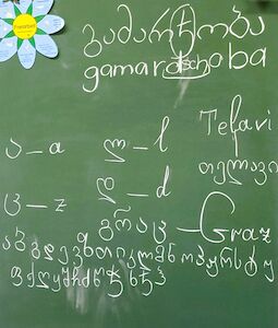 Georgische Schrift und Wörter, einschließlich Gamarjoba, auf einer grünen Tafel.