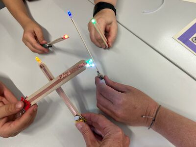Vier Hände halten Bastelstäbe mit kleinen farbigen LED-Lichtern an den Enden.