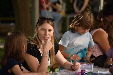 Frau sitzt mit Kindern an einem Tisch und nimmt an einer Aktivität im Freien teil.