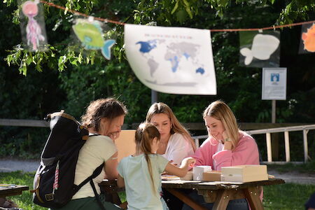 Drei Frauen und ein Mädchen sitzen an einem Picknicktisch und gehen einer Outdoor-Aktivität nach.