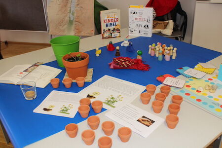 Tisch mit kleinen Blumentöpfen, Papieren, Büchern und bunten Bastelmaterialien.