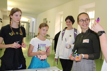 Vier Mädchen stehen zusammen im Haus, halten bunte Bastelutensilien in den Händen und lächeln.
