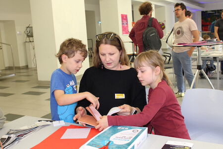 Eine Frau hilft zwei Kindern an einem Tisch in einem Klassenzimmer mit einem Buch.