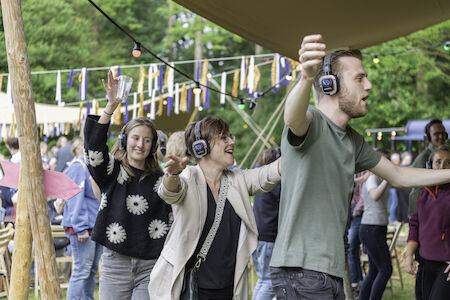 Drei Personen tanzen im Freien und tragen Kopfhörer bei einer festlichen Veranstaltung im Freien.