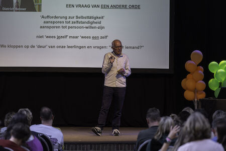 Ein Mann hält auf der Bühne vor einem Publikum mit einer Leinwand und Luftballons eine Präsentation.