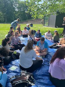 Eine Gruppe von Menschen sitzt im Freien auf einer blauen Plane, schreibt und unterhält sich.