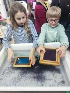 Zwei Kinder verwenden Holzrahmen in einem Wasserbottich für die Papierherstellung.