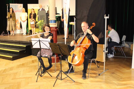 Bei einer Indoor-Veranstaltung spielt eine Frau Flöte und ein Mann Cello auf der Bühne.