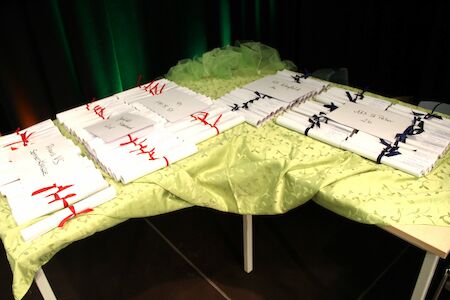 Mit Bändern zusammengebundene Zertifikate liegen auf einem mit grünem Tuch bedeckten Tisch.