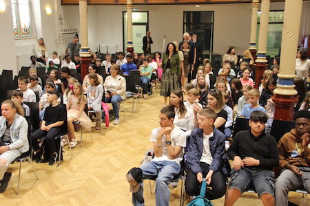 Eine große Gruppe von Studenten sitzt in Stuhlreihen in einer hellen Halle.