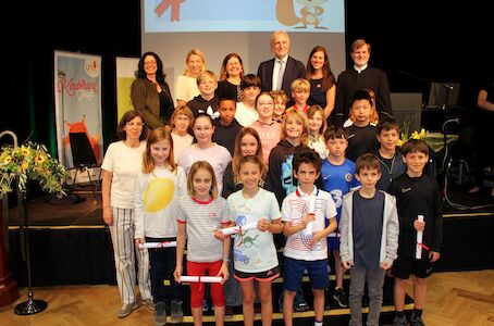 Eine Gruppe von Kindern und Erwachsenen posiert gemeinsam auf der Bühne, einige halten Zertifikate in den Händen.