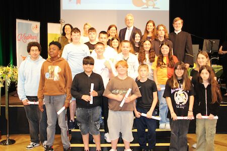 Eine Gruppe von Schülern und Erwachsenen posiert gemeinsam auf der Bühne, einige halten Zertifikate in den Händen.