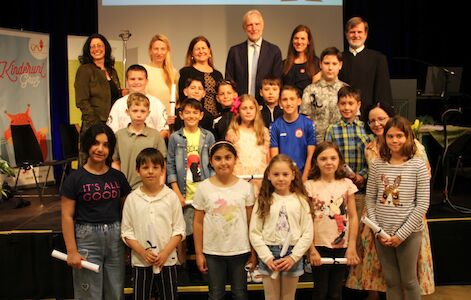 Eine Gruppe von Kindern und Erwachsenen posiert gemeinsam auf der Bühne und lächelt in die Kamera.