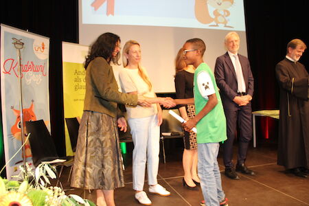 Ein Junge im grünen Hemd schüttelt während einer Veranstaltung einer Frau auf der Bühne die Hand.