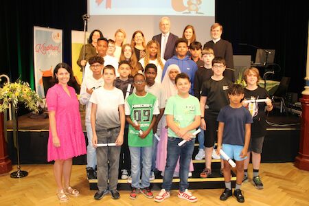 Eine Gruppe von Schülern und Erwachsenen posiert gemeinsam auf einer Bühne, einige halten Zertifikate in den Händen.