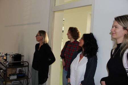 Vier Frauen stehen in einem Raum, blicken auf etwas außerhalb des Bildes und lächeln.