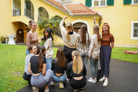 Eine Gruppe junger Frauen posiert gemeinsam vor einem gelben Gebäude.
