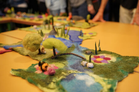 Ein farbenfrohes Filz-Landschaftsdiorama mit Bäumen, einer Brücke und Blumen auf einem Tisch.