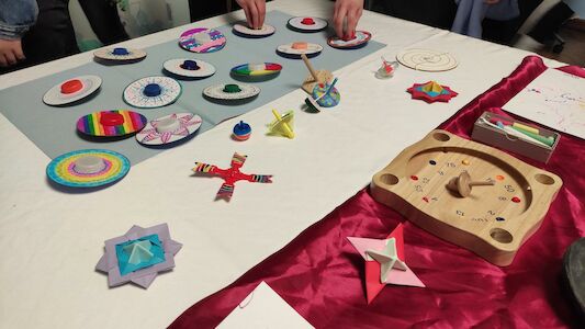 Bunte, handgefertigte Kreisel und Kunsthandwerk werden auf einem Tisch ausgestellt; Hände passen die Teile an.