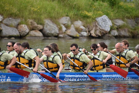 Eine Gruppe von Menschen paddelt mit Schwimmwesten in einem Drachenboot auf einem Fluss.