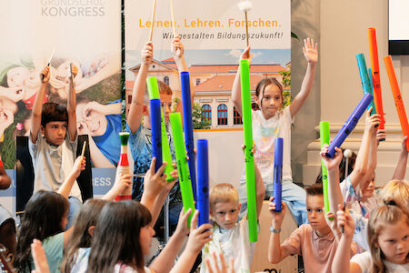 Kinder heben während einer interaktiven Unterrichtsaktivität bunte Röhren und Hände hoch.