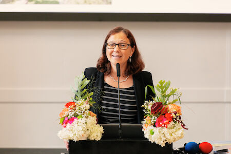 Frau spricht an einem mit bunten Blumen geschmückten Podium.