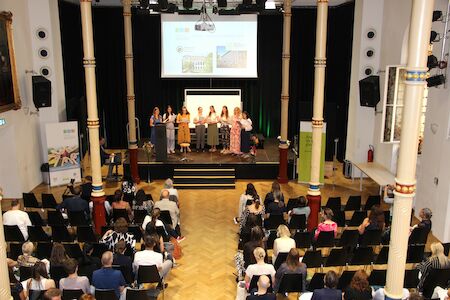 Eine Gruppe von Frauen spricht auf der Bühne zu einem sitzenden Publikum in einem Konferenzsaal.