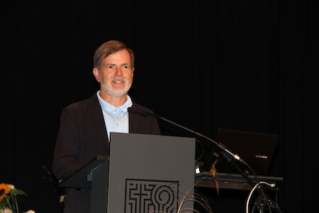 Ein Mann im Anzug spricht an einem Podium mit Mikrofon auf einer dunklen Bühne.
