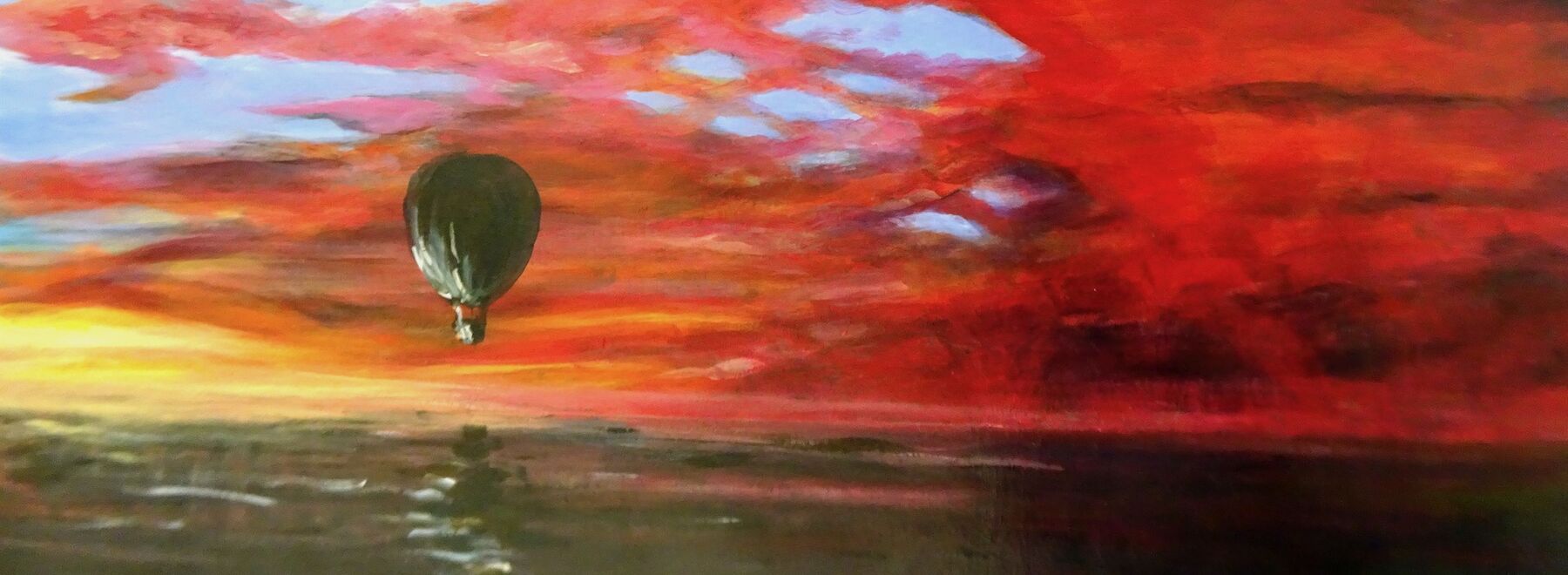 Ein Heißluftballon schwebt unter einem leuchtend roten und orangefarbenen Sonnenuntergangshimmel.
