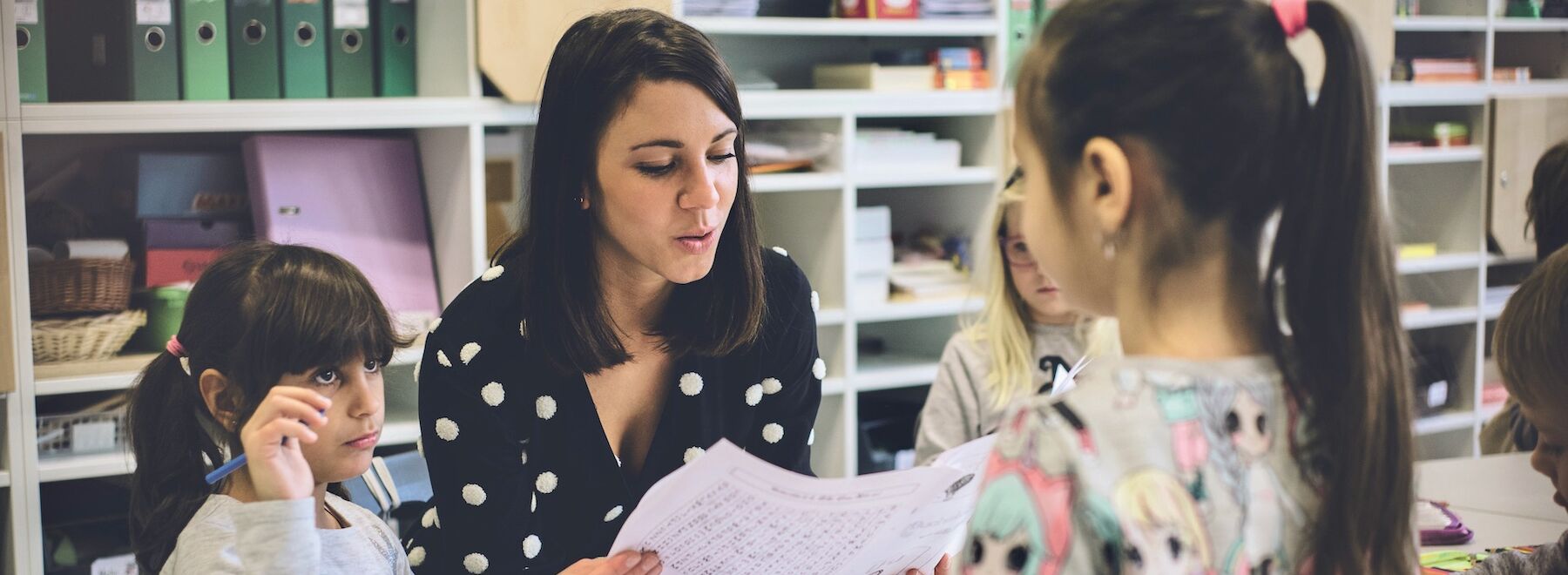 Lehrerin sitzt und lernt mit drei Kindern