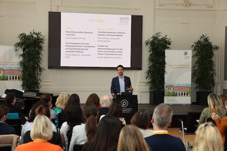 Ein Mann hält in einem Konferenzraum an einem Podium eine Präsentation vor einem Publikum.