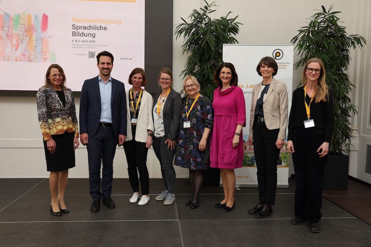 Acht Personen stehen gemeinsam auf einer Bühne bei einer Konferenz zum Thema Sprachbildung.