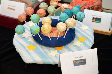 Cake Pops als Planeten dekoriert und auf einem gestreiften Tuch mit gelben Sternen angeordnet.