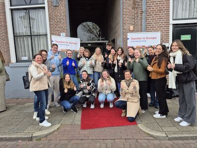 Eine Gruppe von Menschen posiert lächelnd auf einem roten Teppich vor einem Gebäude.