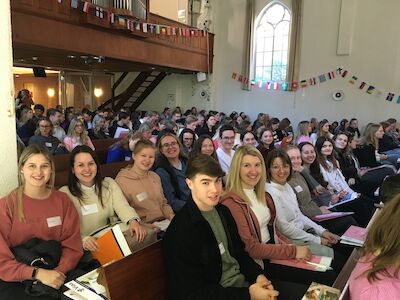Menschen sitzen während einer Veranstaltung in einer Kirchenbank und lächeln in die Kamera.