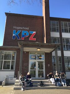 Studenten sitzen vor einem Backsteingebäude mit der Hogeschool KPZ an der Wand.