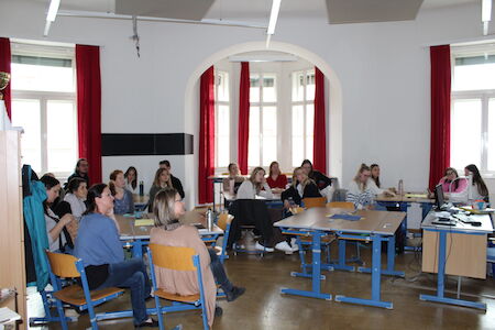 Schüler und Lehrer sitzen in einem Klassenzimmer und hören einer Präsentation oder Unterrichtsstunde zu.