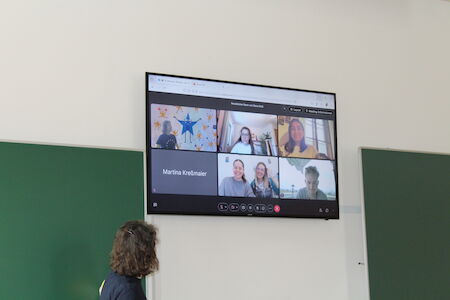 Eine Person blickt auf einen Bildschirm, auf dem ein Gruppenvideoanruf mit sechs Teilnehmern angezeigt wird.
