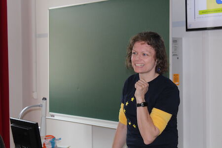Lächelnde Frau, die vor einer leeren Tafel in einem Klassenzimmer steht.