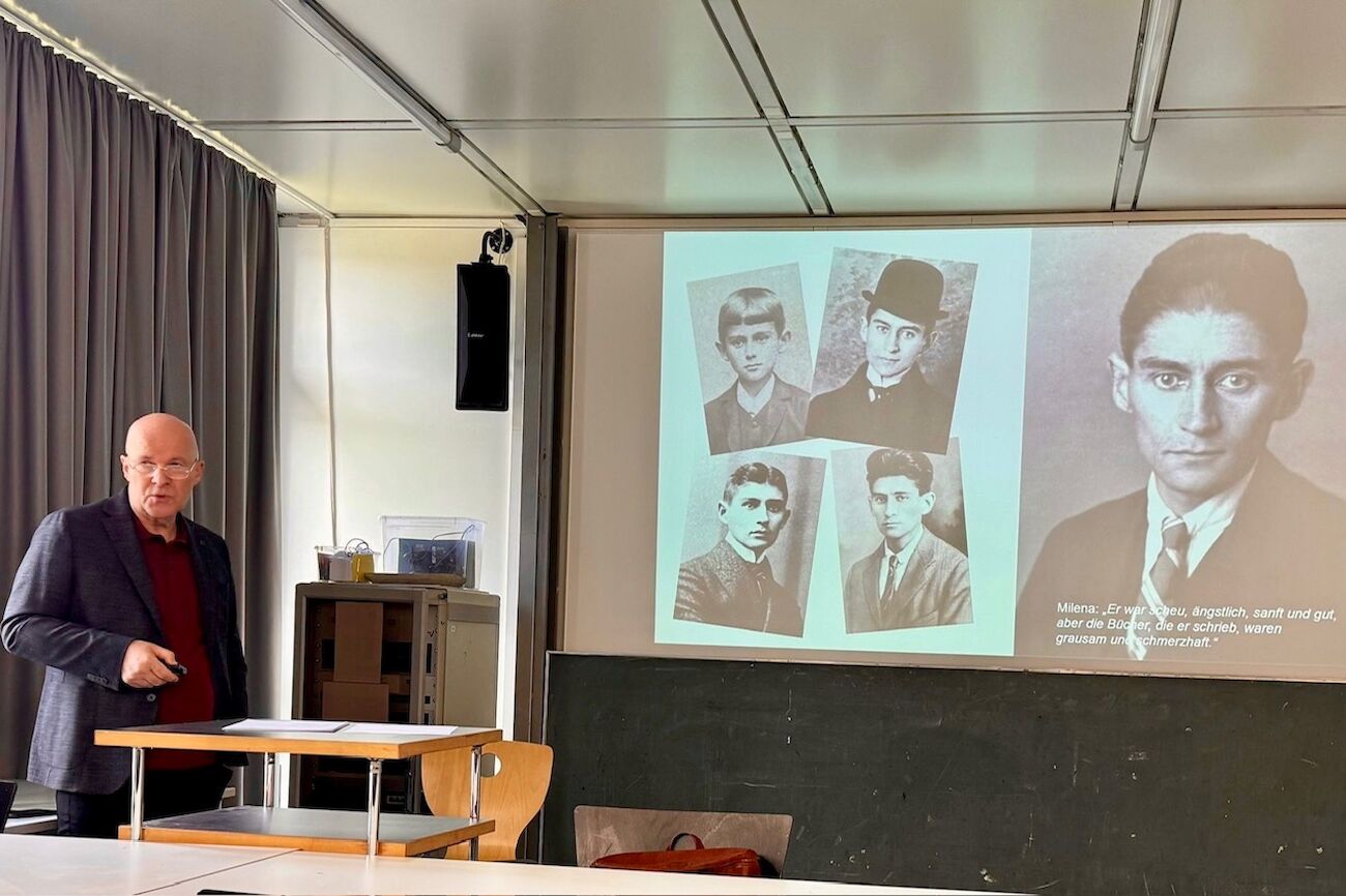 Neben einem Bildschirm präsentiert ein Mann Porträts von Franz Kafka in verschiedenen Altersstufen.