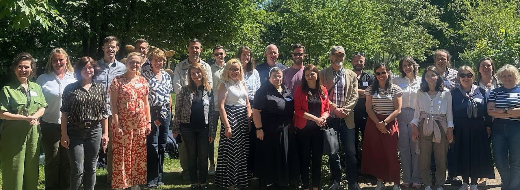Eine Gruppe von Menschen posiert gemeinsam im Freien an einem sonnigen Tag.