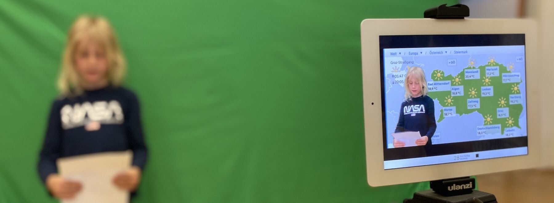 Kind steht vor einem grünen Bildschirm, der als Wetterreporter auf einem Tablet dargestellt wird.