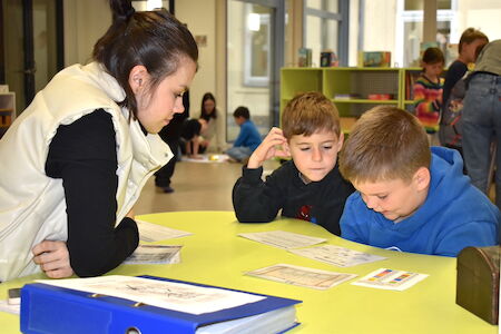 Eine Frau hilft zwei Jungen an einem Tisch in einem Klassenzimmer bei den Schularbeiten.