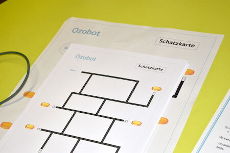 Gedruckte Blätter mit der Aufschrift „Ozobot Schatzkarte“ auf gelbem Untergrund.