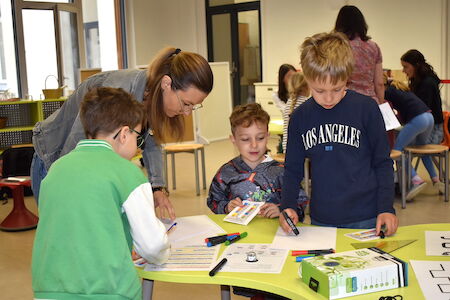 Ein Lehrer hilft drei kleinen Jungen bei einer Zeichenübung an einem Klassentisch.