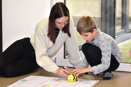 Frau und Junge spielen mit einem gelben Roboter auf einem Gitterdiagramm auf dem Boden.