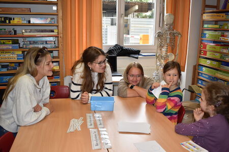 Fünf Personen, darunter Kinder und Erwachsene, sitzen in einem Klassenzimmer um einen Tisch.