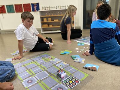 Kinder spielen ein Codierspiel mit Karten und Karten auf dem Klassenzimmerboden.