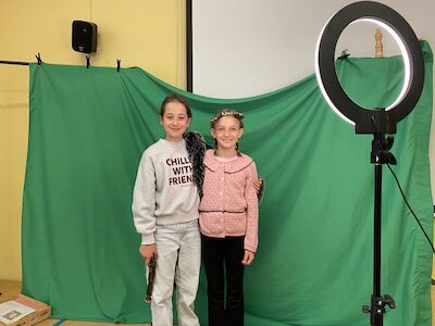Zwei lächelnde Mädchen posieren vor einem Greenscreen mit einem Ringlicht in der Nähe.